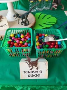 some plastic baskets filled with candy on top of a green cloth covered table next to a sign