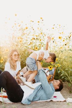 a family laying on the ground in front of sunflowers with one child being held up by his mother