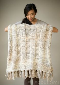 a woman holding up a white knitted blanket with tassels on the ends