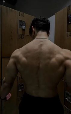 a man standing in front of lockers with his back turned and no shirt on