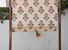 a white and brown patterned roman blind with orange flowers on the outside, hanging from a wooden frame