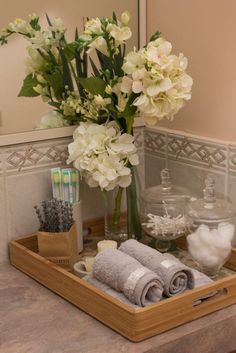 a wooden tray holding towels and flowers on a bathroom counter top with a mirror in the background