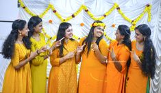 four women in yellow and orange dresses are standing next to each other with their hands together