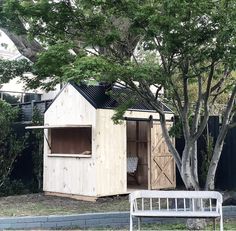 a wooden shed sitting next to a tree in a yard with a bench underneath it