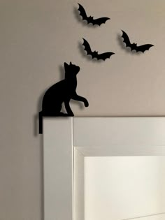 a black cat sitting on top of a white door frame with bats flying around it