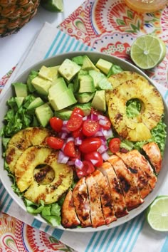 a salad with grilled chicken, avocado, tomatoes and sliced pineapples