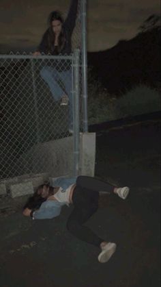 a person laying on the ground in front of a fence with another person standing behind it