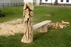 a wooden bench sitting on top of a lush green field next to a pile of logs