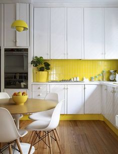 a kitchen with white cabinets and yellow accents on the countertop, along with a wooden dining table surrounded by white chairs