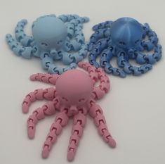 three plastic octopus toys sitting next to each other on a white surface with blue and pink ones