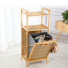 a wooden shelf with clothes and other items in it on the floor next to a plant