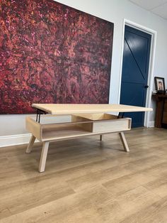 a wooden table sitting on top of a hard wood floor next to a large painting