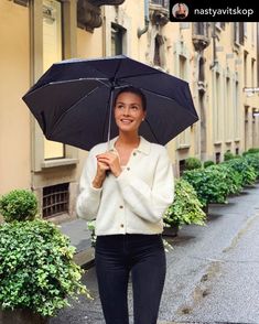 a woman walking down the street with an umbrella in her hand and smiling at the camera