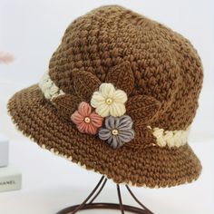 a brown crocheted hat with flowers on it sitting on top of a stand