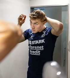 a young man is looking at himself in the mirror and brushing his hair with one hand