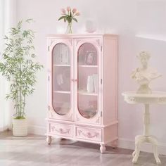 a pink china cabinet sitting next to a table with flowers on it and a potted plant in the corner