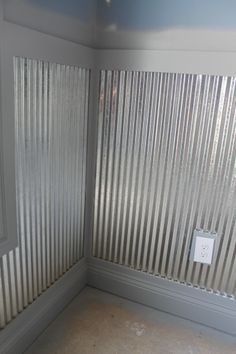 the corner of a room with metal slats on the wall and a light switch