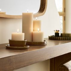 three lit candles sitting on top of a wooden table next to a mirror and tray