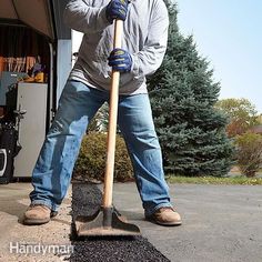 a man holding a shovel while standing next to a pile of black gravel in front of a garage