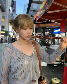 a woman standing next to a food stand holding a cup and looking at something in her hand