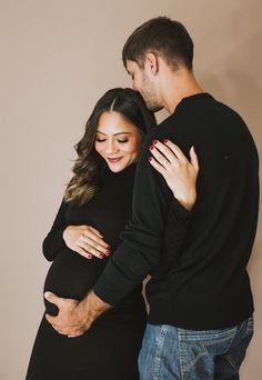 a pregnant couple standing next to each other with their arms wrapped around the baby bump