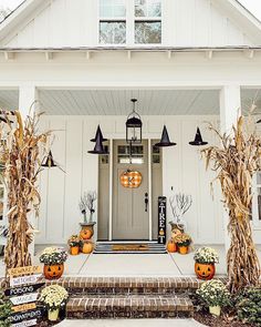 a white house decorated for halloween with pumpkins and corn stalks on the front porch