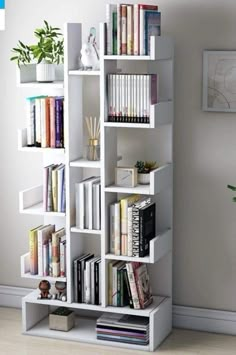 a white book shelf filled with lots of books next to a potted plant on top of a hard wood floor