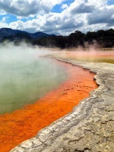 an orange substance floating in the water next to some rocks and trees with mountains in the background