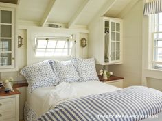 a bed sitting under two windows in a bedroom next to a dresser and window sill