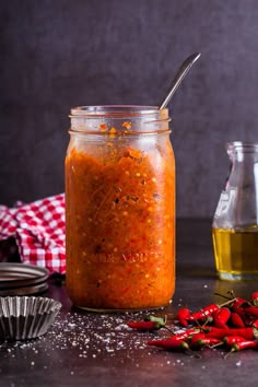 a jar filled with red chili sauce next to other spices and seasonings on a table