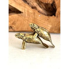 two gold colored fish brooches sitting on top of each other next to a piece of wood