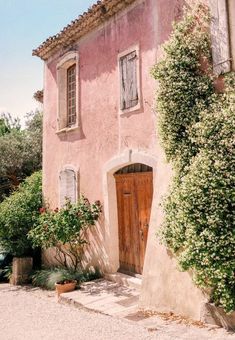 an old pink house with wooden doors and window boxes on the outside, surrounded by greenery