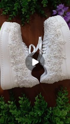 a pair of white high top sneakers with lace and flowers on the side, in front of green leaves