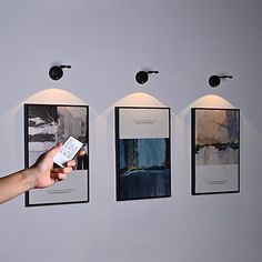 a hand is holding a remote control in front of three pictures on the wall,