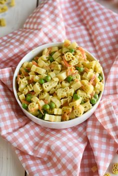 a white bowl filled with pasta and peas on top of a checkered cloth next to two spoons