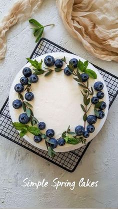 a white cake with blueberries and green leaves on top, sitting on a cooling rack