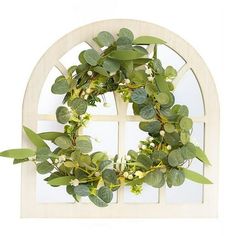 a wreath is hanging on the side of a window with green leaves and white flowers