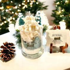 a glass cup filled with marshmallows next to pine cones and christmas trees