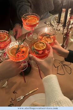 several people toasting with wine glasses filled with orange slices and rosemary sprigs