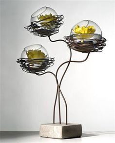 three glass bowls with yellow flowers in them on a metal stand against a white wall