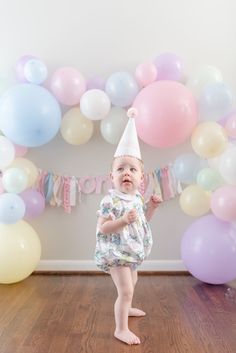 a baby girl wearing a party hat standing in front of balloons with the words spring and pastel inspired 1st birthday party to celebrate your little one's