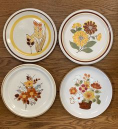 four plates with flowers painted on them sitting on a wooden table next to each other