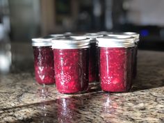 four jars filled with red liquid sitting on top of a granite countertop next to each other