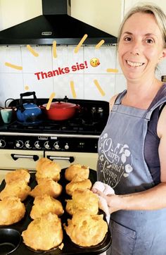 a woman in an apron holding a tray of muffins