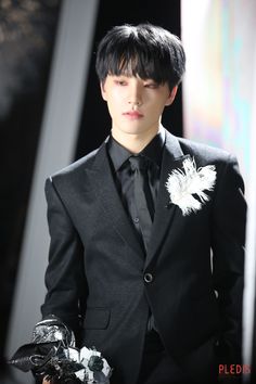 a male model in a black suit and white feather brooch on his lapel