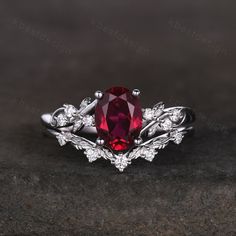 a ring with a red stone surrounded by white diamonds on a black surface in front of a dark background