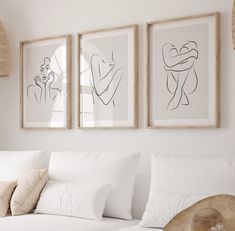 three framed pictures hang on the wall above a white couch in a room with pillows