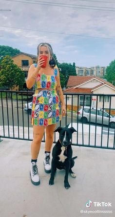 a woman standing next to a black dog on top of a cement ground near a fence