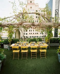 an outdoor dining area with yellow chairs and table set up for dinner on the grass