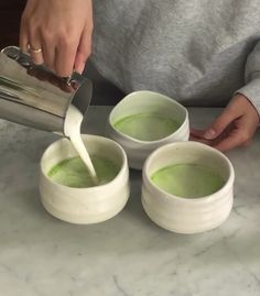 a person pouring green liquid into three bowls